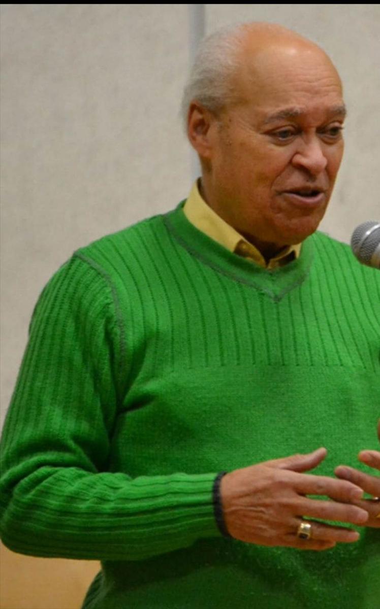 a mand wearing a green sweater speaks at a podium