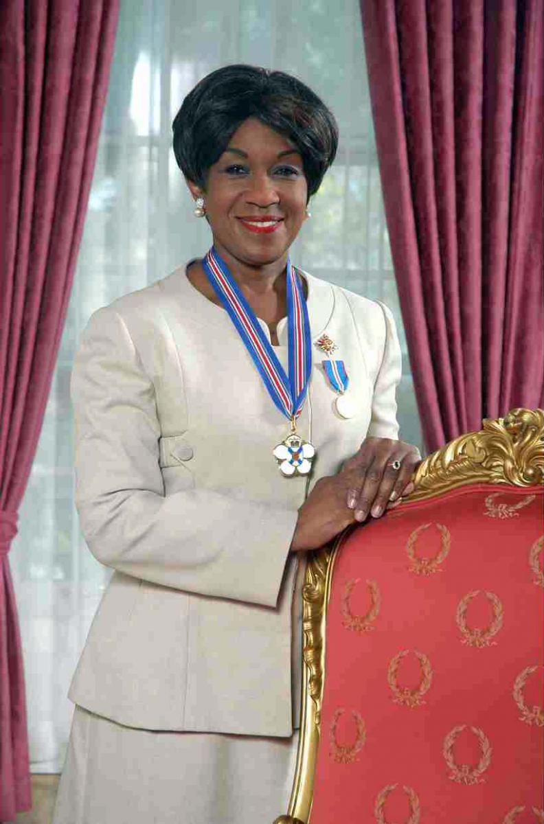 a woman dressed in white smiles sitting on a red sofa wearing a medal around her neck