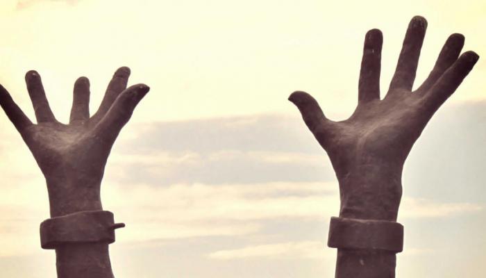 two hands reaching upwards with broken shackles represent the end of enslavement of people of African descent