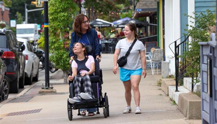 three people one using a wheelchair move through a treed urban park